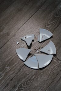close up shot of shards of a broken ceramic plate on a wooden surface