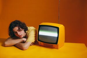 guy in yellow shirt sitting beside a yellow classic tv