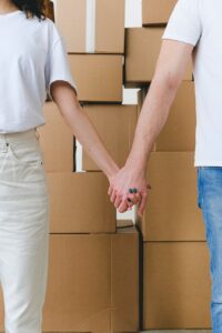 crop couple holding hands near stack of cardboard boxes