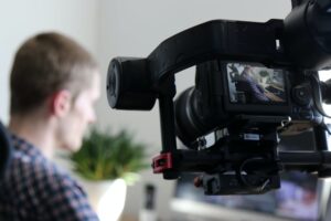 black video camera turn on next to man wears black and gray shirt